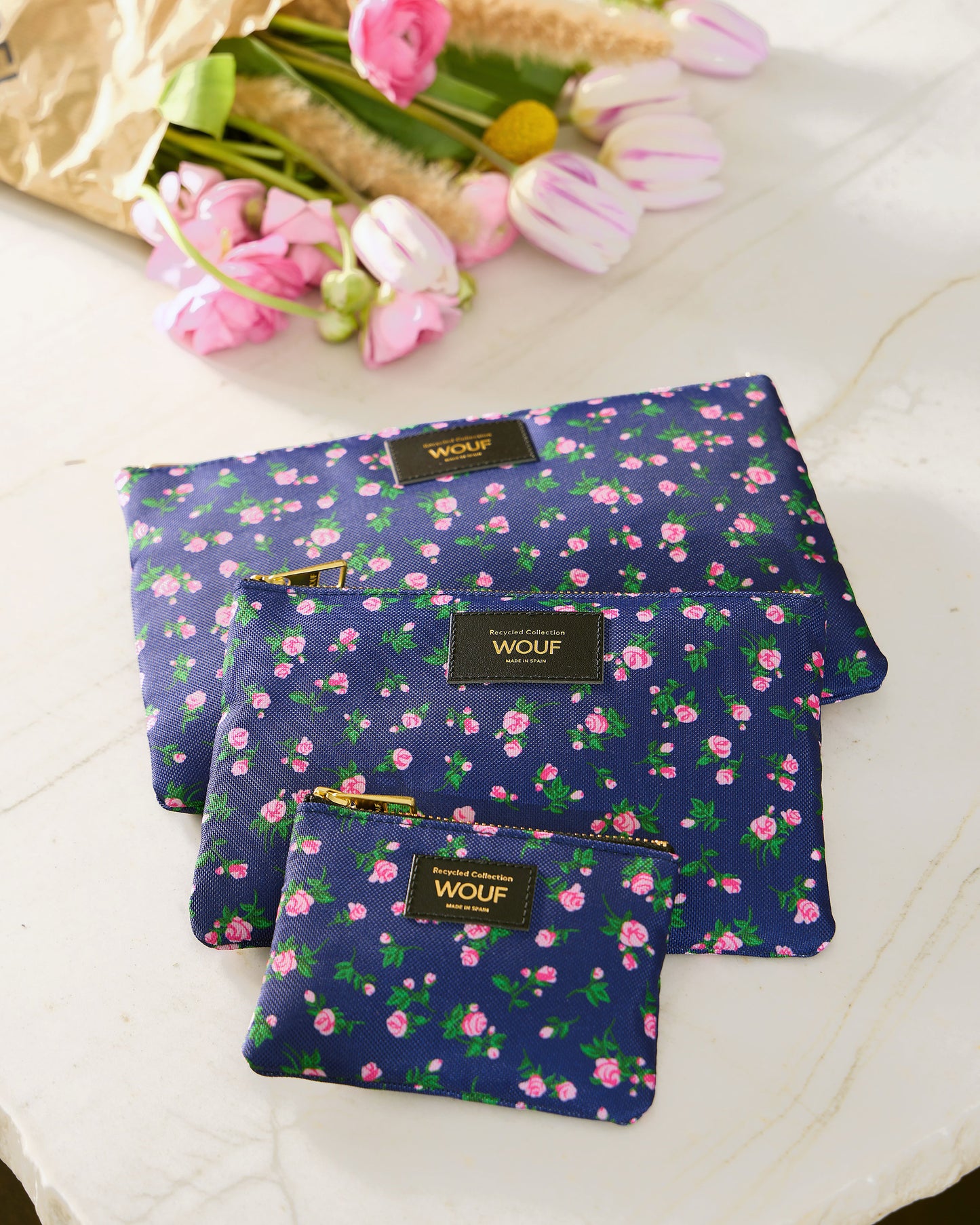 Lifestyle image of the Edith small pouch with pink and green floral print on a navy background - Wouf