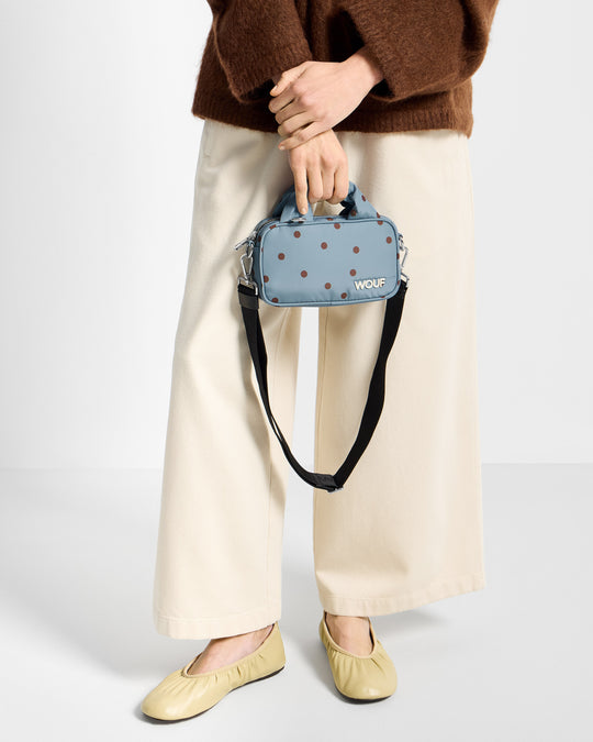 Détail de mannequin avec mini sac à pois marrons sur fond bleu clair - Wouf