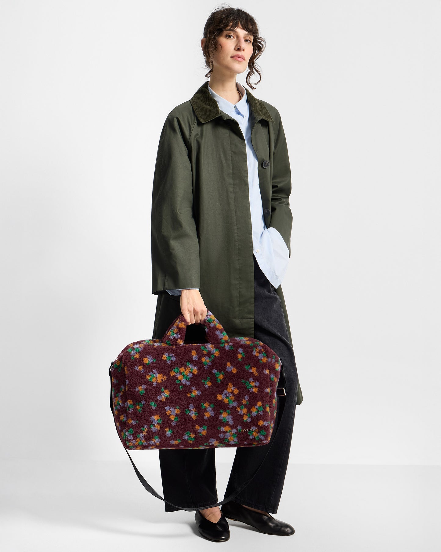 Model with weekend bag in teddy fabric with multicolour floral print on a burgundy background - Wouf